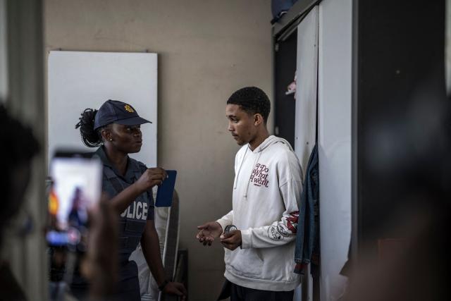 A young man is questioned by a South Africa Police Service (SAPS) officer in his apartment while unseen South African National Defence Force (SANDF) soldiers provide backup during a house search in Westbury, Johannesburg, on March 11, 2026. Soldiers moved into gang-violence hotspots in Johannesburg on March 11, 2026 to support police efforts to tackle rampant crime, described by President Cyril Ramaphosa as one of the biggest threats facing South Africa. (Photo by MARCO LONGARI / AFP)