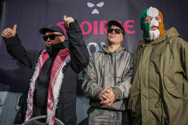 Liam O'Hanna (L), who performs under the stage name Mo Chara with punk-rap group Kneecap, celebrates as he attends a press conference with bandmates Naoise Ó Cairealláin (C), known as Moglai Bap, and JJ O Dochartaigh (R), known as DJ Provaí, at the Conway Mill in Belfast on March 11, 2026. Liam O'Hanna, the Irish-language singer from punk-rap group Kneecap will not face a terrorism charge after UK prosecutors lost a High Court challenge on March 11 against a judge's decision to dismiss the case. (Photo by Paul Faith / AFP)