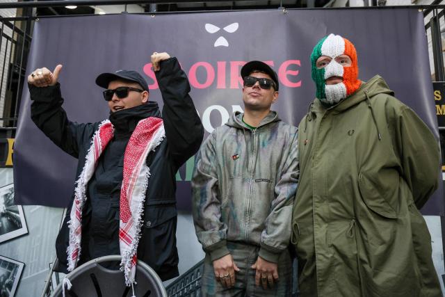 Liam O'Hanna (L), who performs under the stage name Mo Chara with punk-rap group Kneecap, celebrates as he attends a press conference with bandmates Naoise Ó Cairealláin (C), known as Moglai Bap, and JJ O Dochartaigh (R), known as DJ Provaí, at the Conway Mill in Belfast on March 11, 2026. Liam O'Hanna, the Irish-language singer from punk-rap group Kneecap will not face a terrorism charge after UK prosecutors lost a High Court challenge on March 11 against a judge's decision to dismiss the case. (Photo by Paul Faith / AFP)