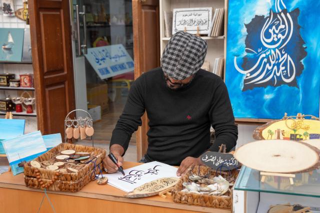 A calligrapher writes a sign outside a shop at a bazaar in Bahrain's capital Manama on March 11, 2026. Iran's Revolutionary Guards said on March 11 that they had targeted several US bases in Kuwait and Bahrain during the war with the United States and Israel. (Photo by AFP) / 