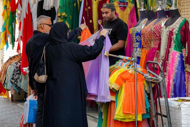 A couple shops for dresses from a vendor at a bazaar in Bahrain's capital Manama on March 11, 2026. Iran's Revolutionary Guards said on March 11 that they had targeted several US bases in Kuwait and Bahrain during the war with the United States and Israel. (Photo by AFP) / 