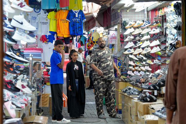 People walk past shoe shops at a bazaar in Bahrain's capital Manama on March 11, 2026. Iran's Revolutionary Guards said on March 11 that they had targeted several US bases in Kuwait and Bahrain during the war with the United States and Israel. (Photo by AFP) / 