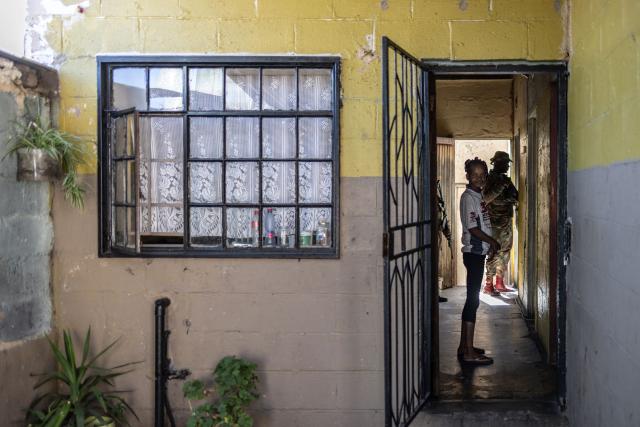 A resident stands in her house as unseen South Africa Police Service (SAPS) officers and South African National Defence Force (SANDF) soldiers conduct a house search in Westbury, Johannesburg, on March 11, 2026. Soldiers moved into gang-violence hotspots in Johannesburg on March 11, 2026 to support police efforts to tackle rampant crime, described by President Cyril Ramaphosa as one of the biggest threats facing South Africa. (Photo by ILARIA FINIZIO / AFP)