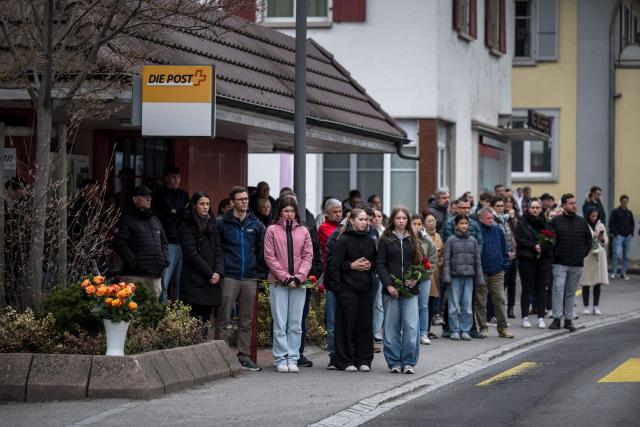 People stand during a memorial ceremony in Kerzers, western Switzerland on March 11, 2026, the day after six people were killed in a bus fire which was seemingly started by a disturbed man on board who set himself alight. (Photo by Fabrice COFFRINI / AFP)