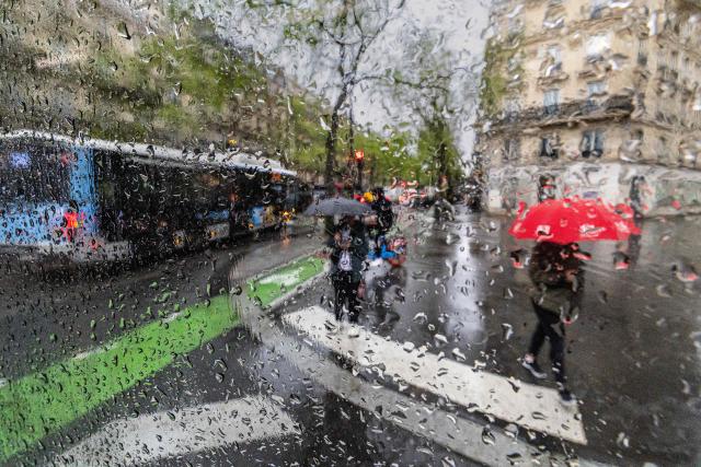 A pedestrian is seen through a window as he walks with an umbrella on a rainy day in Paris on March 11, 2026. (Photo by JOEL SAGET / AFP)