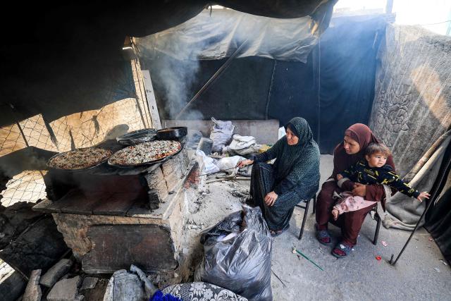 TOPSHOT - Women sit together baking pizza-style pies on a clay oven in one of the tents sheltering Palestinians displaced by conflict in Nuseirat in the central Gaza Strip during the Muslim holy fasting month of Ramadan on March 11, 2026. (Photo by Eyad Baba / AFP)