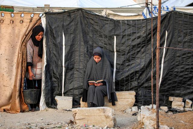 TOPSHOT - A girl sits reading the Quran, Islam's holy book, outside one of the tents sheltering Palestinians displaced by conflict in Nuseirat in the central Gaza Strip during the Muslim holy fasting month of Ramadan on March 11, 2026. (Photo by Eyad Baba / AFP)