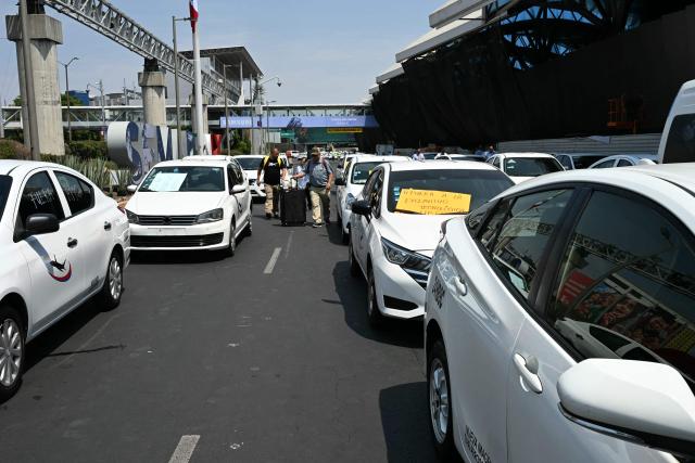 Passengers walk between taxis blocking access to Terminal 2 during a protest against Uber at Mexico City International Airport in Mexico City on March 11, 2026. (Photo by YURI CORTEZ / AFP)
