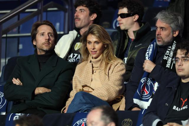 French producer Mathieu Vergne (L) and French TV host Ophelie Meunier (C) sit in the stands ahead of the UEFA Champions League round of 16 first leg football match between Paris Saint-Germain (PSG) and Chelsea at the Parc des Princes stadium in Paris on March 11, 2026. (Photo by FRANCK FIFE / AFP)
