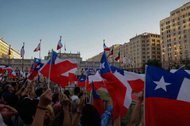 Supporters of Chile's new President Jose Antonio Kast wave national flags outside La Moneda palace in Santiago on March 11, 2026. Chile's most right-wing president in over three decades, Jose Antonio Kast, takes office on March 11, 2026, on a promise to tackle surging rates of violent crime and carry out mass migrant deportations. (Photo by Raul BRAVO / AFP)