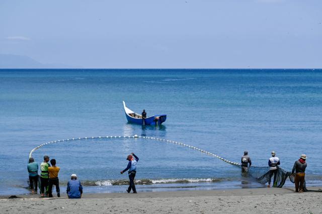 Fishermen pull a net at a beach in Banda Aceh on March 12, 2026. (Photo by CHAIDEER MAHYUDDIN / AFP)