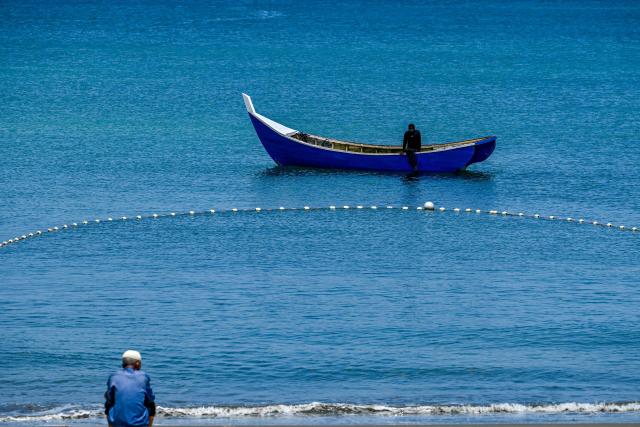 A man looks at a fisherman on his boat at a beach in Banda Aceh on March 12, 2026. (Photo by CHAIDEER MAHYUDDIN / AFP)