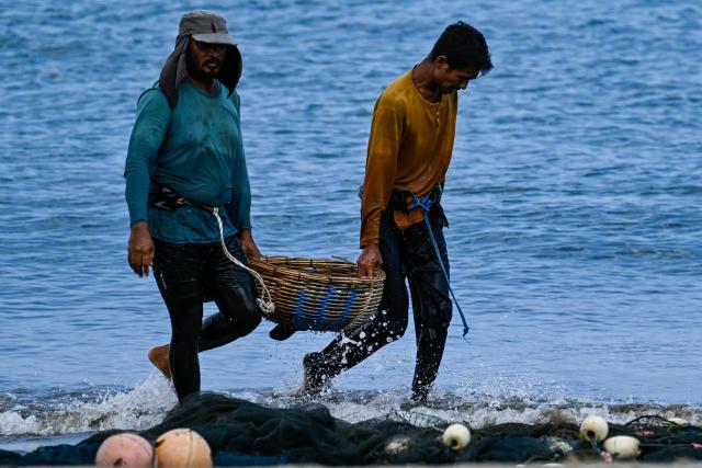 Fishermen carry a basket of fish at a beach in Banda Aceh on March 12, 2026. (Photo by CHAIDEER MAHYUDDIN / AFP)