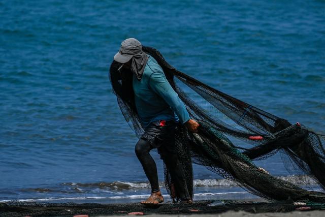 A fisherman pulls a net to clean at a beach in Banda Aceh on March 12, 2026. (Photo by CHAIDEER MAHYUDDIN / AFP)