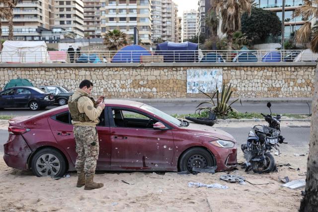 TOPSHOT - A soldier inspects damaged vehicles at the site of an Israeli airstrike on the seaside area of Ramlet al-Bayda in Beirut, with tents sheltering displaced people visible in the background, on March 12, 2026. Lebanon said an Israeli strike on central Beirut's seafront killed at least seven people early on March 12, another attack in the heart of the capital as Iran-backed Hezbollah launched more missiles at Israel. (Photo by Anwar AMRO / AFP)