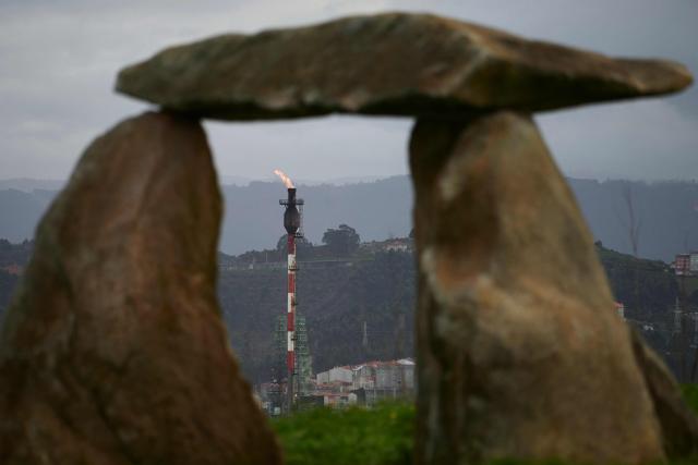 A gas flare is pictured through a dolmen-shape sculpture at the Repsol oil refinery in A Coruna, northwestern Spain, on March 11, 2026. The US-Israeli war on Iran has expanded across the Gulf and beyond, upending global energy markets and trade, and virtually halting traffic in the Strait of Hormuz, through which a fifth of the world's crude oil travels. The 32 member countries of the International Energy Agency (IEA) decided to unlock 400 million barrels of oil from their reserves - the biggest such release ever- to ease the impact of the Middle East war. (Photo by MIGUEL RIOPA / AFP)