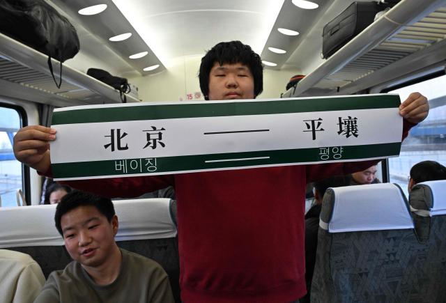 A man holds a banner reading 'Beijing-Pyongyang' onboard the K27 train bound for Pyongyang at Beijing Railway Station in Beijing on March 12, 2026. A passenger train that departed from the northeastern Chinese city of Dandong arrived in the North Korean capital Pyongyang on March 12, as rail service between the neighbouring countries resumed after six years. (Photo by ADEK BERRY / AFP)