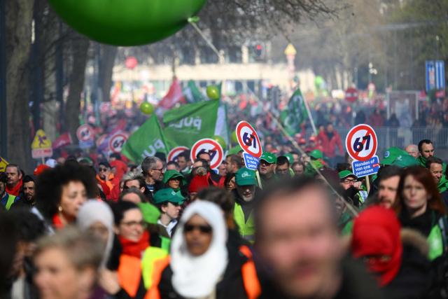 Protesters hold signs as they take part in a demonstration during a national day of action against the austerity plan of the federal Arizona government, in Brussels on March 12, 2026. Belgium will be running at a slower pace on March 12, 2026 due to a call for a strike by the country’s three main trade unions, resulting in the suspension of all traffic at Charleroi Airport and the cancellation of departing flights from Brussels-Zaventem. (Photo by Nicolas TUCAT / AFP)