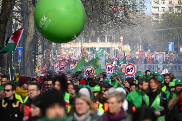 Protesters hold signs as they take part in a demonstration during a national day of action against the austerity plan of the federal Arizona government, in Brussels on March 12, 2026. Belgium will be running at a slower pace on March 12, 2026 due to a call for a strike by the country’s three main trade unions, resulting in the suspension of all traffic at Charleroi Airport and the cancellation of departing flights from Brussels-Zaventem. (Photo by Nicolas TUCAT / AFP)