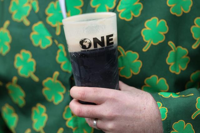 A racegoer drinks a pint of Guinness to mark 'St Patrick's Thursday' with an Irish them, on the third day of the Cheltenham Festival at Cheltenham Racecourse, in Cheltenham, western England on March 12, 2026. (Photo by Adrian Dennis / AFP)