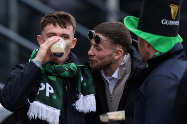 A racegoer (L) drinks a pint of Guinness to mark 'St Patrick's Thursday' with an Irish them, on the third day of the Cheltenham Festival at Cheltenham Racecourse, in Cheltenham, western England on March 12, 2026. (Photo by Adrian Dennis / AFP)