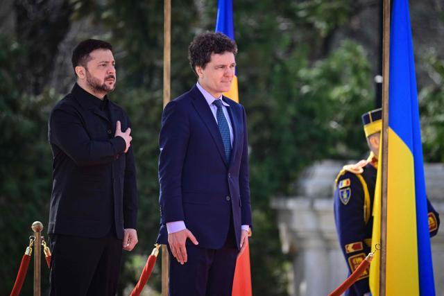 Romanian President Nicusor Dan (R) and his Ukrainian counterpart Volodymyr Zelensky listen to the national anthems during an official welcoming ceremony at Cotroceni Palace, the official residence of the Romanian president, in Bucharest on March 12, 2026. Ukrainian President Zelensky arrived on March 12 in Romania, where he was to visit an F-16 fighter jet training centre and meet Romania's leader, before visiting France later this week. The visits come at a time of uncertainty over planned peace talks between Kyiv and Moscow that have been spearheaded by the United States and derailed by the US-Israeli war with Iran. (Photo by Daniel MIHAILESCU / AFP)