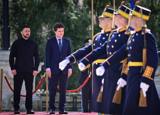 Romanian President Nicusor Dan (2L) and his Ukrainian counterpart Volodymyr Zelensky review a military honour guard during an official welcoming ceremony at Cotroceni Palace, the official residence of the Romanian president, in Bucharest on March 12, 2026. Ukrainian President Zelensky arrived on March 12 in Romania, where he was to visit an F-16 fighter jet training centre and meet Romania's leader, before visiting France later this week. The visits come at a time of uncertainty over planned peace talks between Kyiv and Moscow that have been spearheaded by the United States and derailed by the US-Israeli war with Iran. (Photo by Daniel MIHAILESCU / AFP)