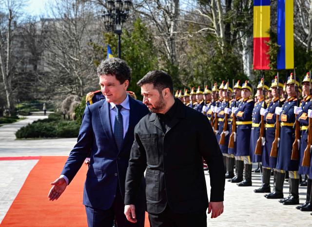 Romanian President Nicusor Dan (L) and his Ukrainian counterpart Volodymyr Zelensky review an honour guard during an official welcoming ceremony at Cotroceni Palace, the official residence of the Romanian president, in Bucharest on March 12, 2026. Ukrainian President Zelensky arrived on March 12 in Romania, where he was to visit an F-16 fighter jet training centre and meet Romania's leader, before visiting France later this week. The visits come at a time of uncertainty over planned peace talks between Kyiv and Moscow that have been spearheaded by the United States and derailed by the US-Israeli war with Iran. (Photo by Daniel MIHAILESCU / AFP)