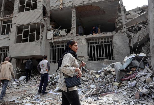 A woman stands in front of a destroyed residential building as residents collect their belongings from the rubble in Tehran on March 12, 2026. The United States and Israel started striking Iran on February 28, killing the Iranian supreme leader and top military leaders, and prompting authorities to retaliate with strikes on Israel and across the Gulf. (Photo by AFP) / 