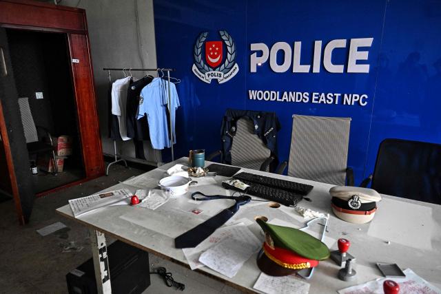 A room imitating a Singaporean police station is seen inside an abandoned scam centre in O'Smach town on the Thai-Cambodian border on March 12, 2026, during a press trip organised by Thailand's Ministry of Foreign Affairs and the Royal Thai Army. Broken computer monitors in bombed-out offices, scattered fake police uniforms, phony hundred dollar bills, Chinese tea tables: these were the vestiges of a frantic escape of suspected cyberscammers fleeing a resort on the Cambodia-Thailand border. (Photo by Lillian SUWANRUMPHA / AFP) / To go with 'THAILAND-CAMBODIA-CONFLICT-CYBERCRIME,FOCUS' by Chayanit ITTHIPONGMAETEE and Sally JENSEN