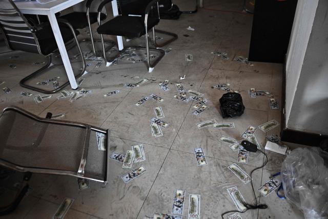 Fake US dollar bills lie on the floor inside an abandoned scam centre in O'Smach town on the Thai-Cambodian border on March 12, 2026, during a press trip organised by Thailand's Ministry of Foreign Affairs and the Royal Thai Army. Broken computer monitors in bombed-out offices, scattered fake police uniforms, phony hundred dollar bills, Chinese tea tables: these were the vestiges of a frantic escape of suspected cyberscammers fleeing a resort on the Cambodia-Thailand border. (Photo by Lillian SUWANRUMPHA / AFP) / To go with 'THAILAND-CAMBODIA-CONFLICT-CYBERCRIME,FOCUS' by Chayanit ITTHIPONGMAETEE and Sally JENSEN