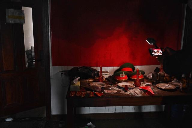 Members of the media record replica Vietnamese police hats inside an abandoned scam centre in O'Smach town on the Thai-Cambodian border on March 12, 2026, during a press trip organised by Thailand's Ministry of Foreign Affairs and the Royal Thai Army. Broken computer monitors in bombed-out offices, scattered fake police uniforms, phony hundred dollar bills, Chinese tea tables: these were the vestiges of a frantic escape of suspected cyberscammers fleeing a resort on the Cambodia-Thailand border. (Photo by Lillian SUWANRUMPHA / AFP) / To go with 'THAILAND-CAMBODIA-CONFLICT-CYBERCRIME,FOCUS' by Chayanit ITTHIPONGMAETEE and Sally JENSEN