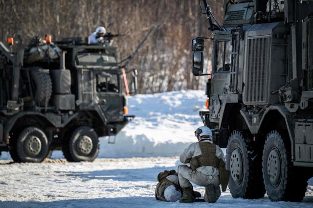 A member of the Norwegian army Combat Support Battalion looks over a wounded comrade, as another one returns fire during an attack simulation on a logistics unit near Setermoen on March 12, 2026, as NATO conducts its Cold Response military exercise. The Norwegian-led winter exercise involves 32.000 troops, 100 aircraft, and 30 warships from 14 nations taking part in high intensity, multi-domain operations in an arctic climate. (Photo by John MACDOUGALL / AFP)