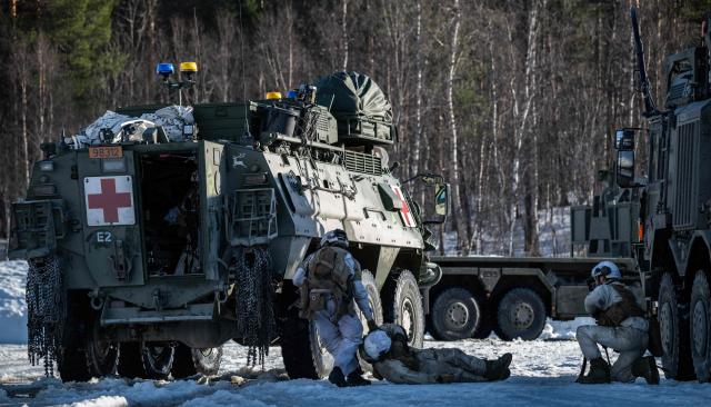 A Norwegian army medic drags a wounded comrade from the Norwegian army Combat Support Battalion towards a Patria Pasi APC after he was wounded during an attack simulation on a logistics unit near Setermoen on March 12, 2026, as NATO conducts its Cold Response military exercise. The Norwegian-led winter exercise involves 32.000 troops, 100 aircraft, and 30 warships from 14 nations taking part in high intensity, multi-domain operations in an arctic climate. (Photo by John MACDOUGALL / AFP)