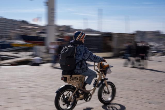A man rides an electric bicycle in the old harbor Marseille, southern France, on March 12, 2026. (Photo by Elodie CLEMENT / AFP)