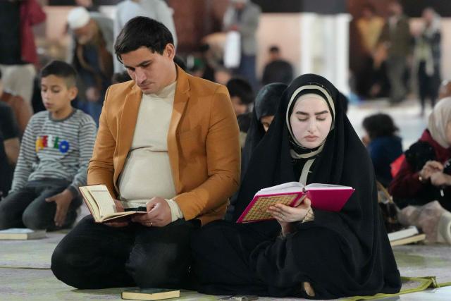 A Shia Muslim man and woman recite from a copy of the Koran, Islam's holy book, as they participate in the ritual of itikaf, or spiritual retreat, at the Kufa Mosque, taking advantage of the days and nights of Laylat al-Qadr, or the Night of Destiny, one of the holiest nights during the fasting month of Ramadan, in the holy city of Kufa, south of the Iraqi capital Baghdad on March 12, 2026. (Photo by Qassem al-KAABI / AFP)
