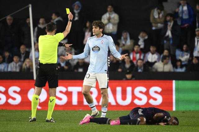 Belgian referee Erik Lambrechts shows a yellow card to Celta Vigo's Spanish defender #20 Marcos Alonso Mendoza next to Lyon's Brazilian forward #09 Endrick (down) during the UEFA Europa League last 16 first leg football match between RC Celta de Vigo and Olympique Lyonnais (OL) at Balaidos Stadium in Vigo on March 12, 2026. (Photo by Miguel RIOPA / AFP)