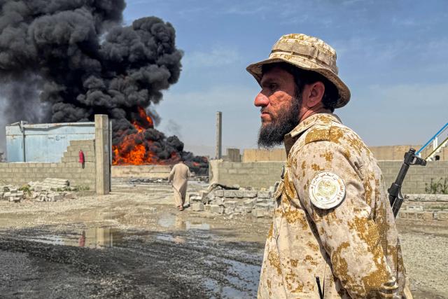TOPSHOT - A Taliban security personnel stands guard as smoke rises from the site after overnight Pakistani airstrikes hit oil depots for commercial airlines, near the Kandahar airport in the Daman district of Kandahar province on March 13, 2026. Afghan authorities said on March 13 that Pakistan attacks on Kabul and border provinces killed four people in the capital and two in the east, the latest deadly clashes in the long-running conflict. (Photo by AFP)