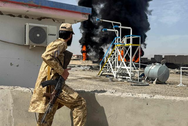 A Taliban security personnel keeps watch as smoke rises from the site after overnight Pakistani airstrikes hit oil depots for commercial airlines, near the Kandahar airport in the Daman district of Kandahar province on March 13, 2026. Afghan authorities said on March 13 that Pakistan attacks on Kabul and border provinces killed four people in the capital and two in the east, the latest deadly clashes in the long-running conflict. (Photo by AFP)