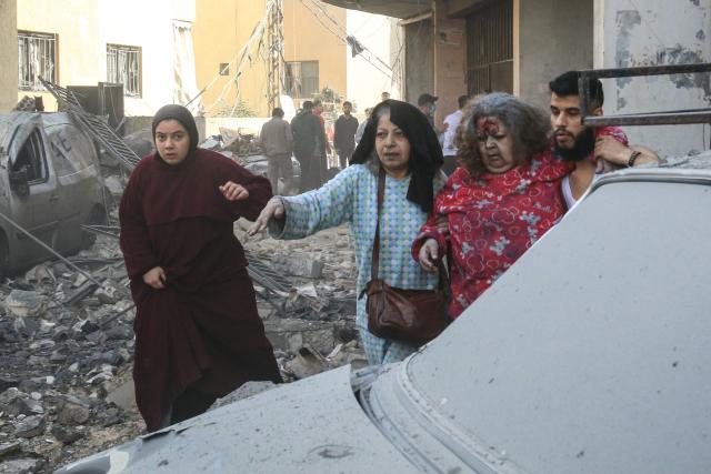 TOPSHOT - An injured woman is helped away from the site of an Israeli airstrike that targeted a neighborhood in the town of Mieh Mieh, some five kilometers east of the southern Lebanese city of Sidon on March 13, 2026. Israel continued striking Beirut as it threatened to expand operations and seize territory in Lebanon if the militant group Hezbollah did not stop its attacks. (Photo by Mahmoud ZAYYAT / AFP)
