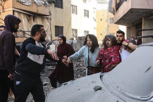 An injured woman is helped away from the site of an Israeli airstrike that targeted a neighborhood in the town of Mieh Mieh, some five kilometers east of the southern Lebanese city of Sidon on March 13, 2026. Israel continued striking Beirut as it threatened to expand operations and seize territory in Lebanon if the militant group Hezbollah did not stop its attacks. (Photo by Mahmoud ZAYYAT / AFP)