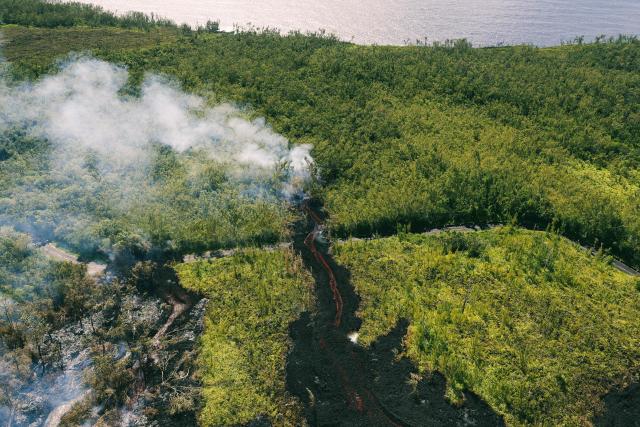 This aerial photograph shows a lava flow making its way through a forested area crossing the RN2 road near Sainte-Rose close to the Piton de la Fournaise volcano in the southeast of the French overseas island of Reunion on March 13, 2026. Two lava flows spewed out by Piton de la Fournaise, a volcano that has been erupting for a month on Rйunion Island, have cut the national road linking the south to the east of the island—something that has not happened in nearly 20 years, the prefecture said on Friday. (Photo by Richard BOUHET / AFP)