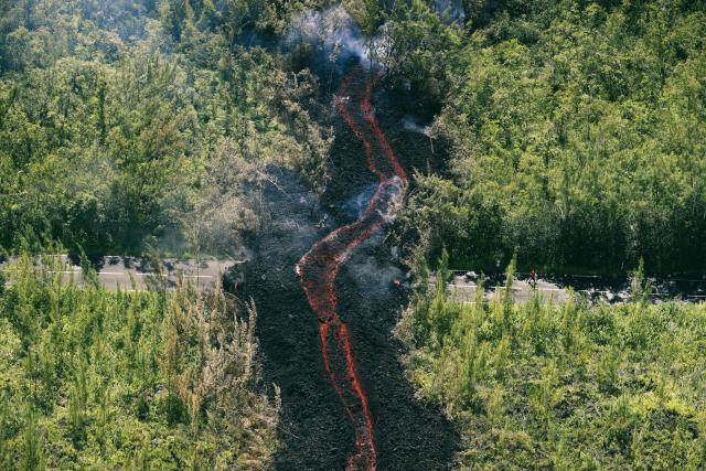 This aerial photograph shows a lava flow making its way through a forested area crossing the RN2 road near Sainte-Rose close to the Piton de la Fournaise volcano in the southeast of the French overseas island of Reunion on March 13, 2026. Two lava flows spewed out by Piton de la Fournaise, a volcano that has been erupting for a month on Rйunion Island, have cut the national road linking the south to the east of the island—something that has not happened in nearly 20 years, the prefecture said on Friday. (Photo by Richard BOUHET / AFP)