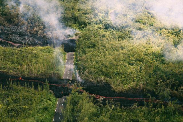 This aerial photograph shows a lava flow making its way through a forested area crossing the RN2 road near Sainte-Rose close to the Piton de la Fournaise volcano in the southeast of the French overseas island of Reunion on March 13, 2026. Two lava flows spewed out by Piton de la Fournaise, a volcano that has been erupting for a month on Rйunion Island, have cut the national road linking the south to the east of the island—something that has not happened in nearly 20 years, the prefecture said on Friday. (Photo by Richard BOUHET / AFP)