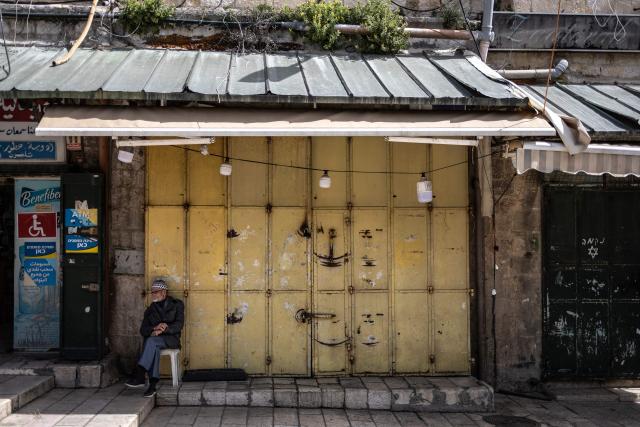 TOPSHOT - A man sits in front of a closed shop in the Old City of Jerusalem on March 13, 2026. New waves of attacks struck Iran and Gulf nations on March 13 after Tehran renewed its threats on oil facilities, while France announced its first soldier killed during the Mideast war. The latest strikes on Iran hit over 200 targets in the past day, Israel's military said well into the second week of the US-Israeli campaign that has grown into a deadly regional fight causing economic chaos. (Photo by OLYMPIA DE MAISMONT / AFP) / 