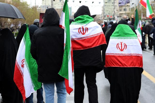 Iranians with their national flag draped across their shoulders take part in the Al-Quds (Jerusalem) Day rally, a commemoration in support of the Palestinian people on the last Friday of the Islamic holy month of Ramadan, in Tehran on March 13, 2026. On February 28, Israel and the United States launched strikes on Iran, killing its supreme leader Ayatollah and triggering a war that spread across the Middle East. (Photo by AFP) / 
