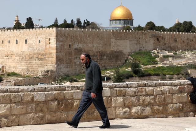A Palestinian man walks along a street on the last Friday noon prayer of the Muslim holy fasting month of Ramadan, in east Jerusalem's neighbourhood of Ras al-Amud, on March 13, 2026, as the site al-Aqsa mosque and the Dome of the Rock (background) is closed since the US-Israel war with Iran started on February 28. (Photo by Ahmad GHARABLI / AFP)