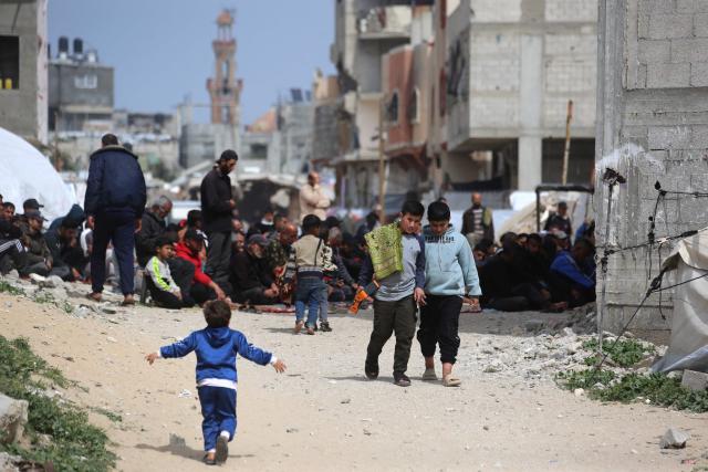 Palestinian boys walk with their pray mat as Muslim men pray during the last Friday noon prayer of the Muslim holy fasting month of Ramadan, outside the Al-Talbani Mosque, destroyed by the Israeli military in Khan Yunis, in the southern Gaza Strip on  March 13, 2026. (Photo by Bashar Taleb / AFP)