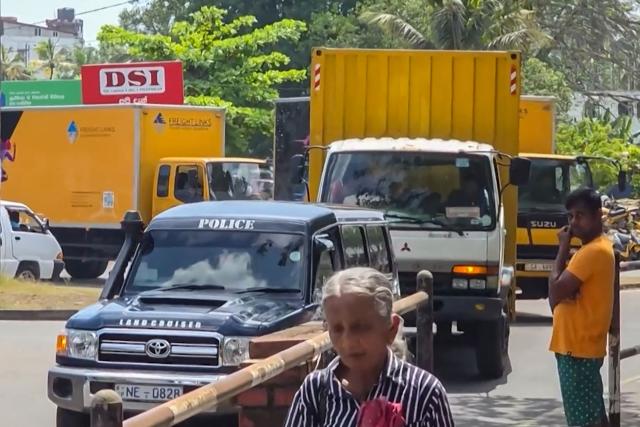 This frame grab from AFPTV video footage taken on March 13, 2026 shows police vehicle escorting a convoy of trucks carrying the remains of 84 Iranian sailors from Galle hospital ahead of their repatriation, who perished when their frigate was sunk nine days ago by a US submarine off the coast of Sri Lanka. The seamen were killed when IRIS Dena was torpedoed on March 4 just off the coast of Sri Lanka, in a move that extended the Middle East war to the Indian Ocean. (Photo by AFPTV / AFP)