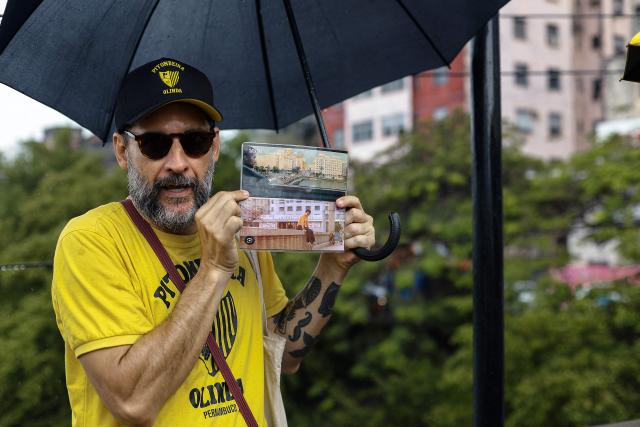 Tourist guide Roderick shows a picture form the film "O Agente Secreto" (The Secret Agent) during a guided tour through the scenarios of the film at the city center of Recife, Pernambuco state, Brazil, on February 13, 2026. The northeastern Brazilian city of Recife, where the Oscar-nominated movie "The Secret Agent" is set, is revelling in its moment in the limelight as tourists flock to film locations and a classic local shirt flies off the shelves. (Photo by BRENDA ALCANTARA / AFP)